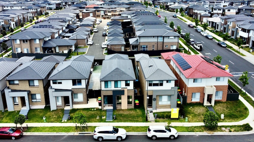 Aerial shot of dozens of houses in neat rows in a new outer-suburban housing estate.