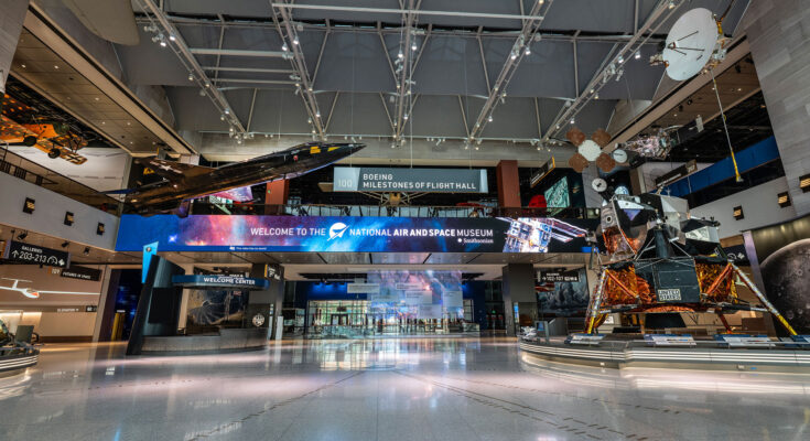 a museum gallery with a wide open space at its center, aircraft suspended from the ceiling and spacecraft standing on the floor