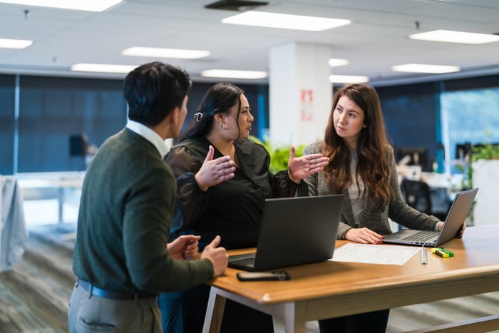 Tres personas que tienen una discusión en una mesa con una computadora.