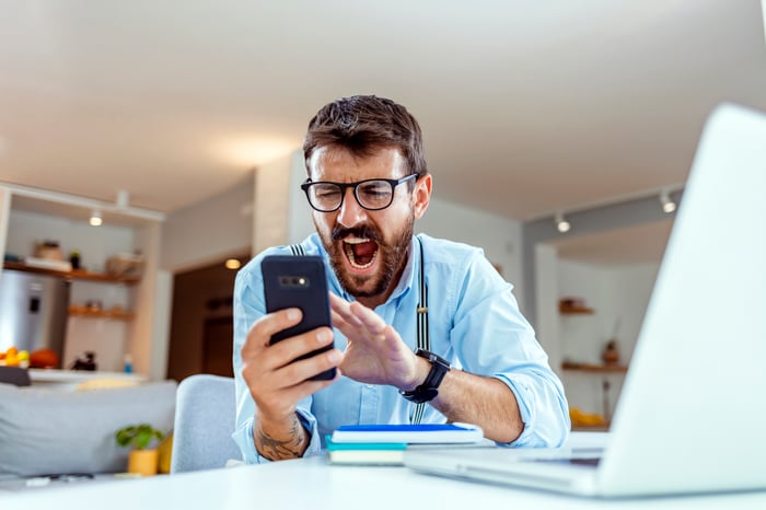 Un desafortunado inversor que mira un teléfono inteligente en una oficina en casa.
