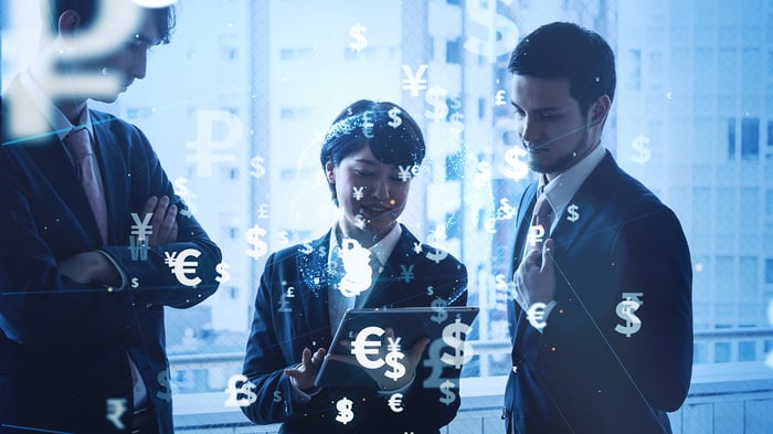 Las personas que miran la tableta con símbolos de moneda digital como dólares, euros y yenes flotando.