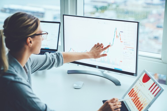 Una mujer señala un gráfico de inversiones en una pantalla sobre su escritorio.