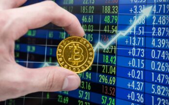 Hand holding gold Bitcoin beside an upward arrow on a trading screen.