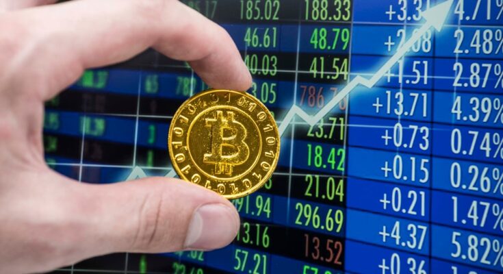 Hand holding gold Bitcoin beside an upward arrow on a trading screen.