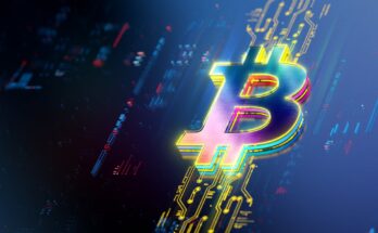 A Bitcoin logo rests on a lit up portion of a screen displaying price data.