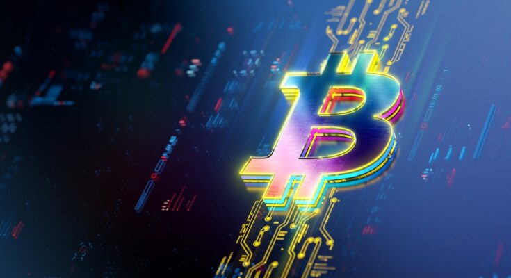 A Bitcoin logo rests on a lit up portion of a screen displaying price data.