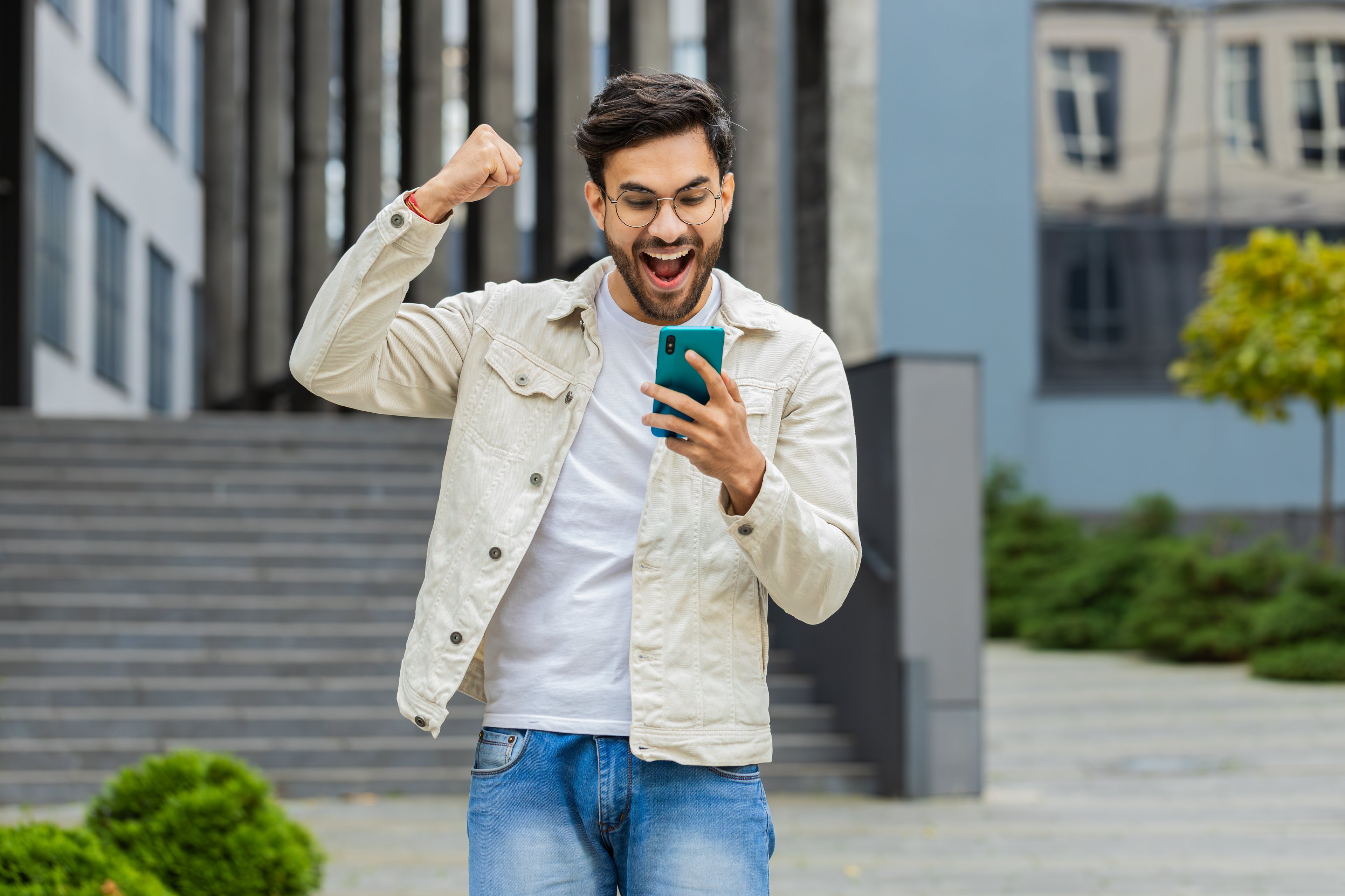 Un joven inversor sostiene un teléfono inteligente y celebra.