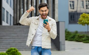 Young investor holding smartphone and celebrating.