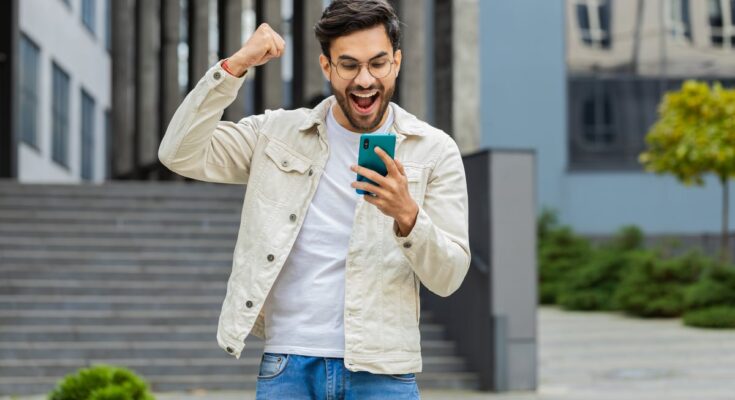 Young investor holding smartphone and celebrating.