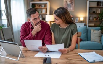 A couple sit at a table in their home looking at papers.