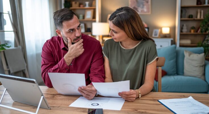 A couple sit at a table in their home looking at papers.
