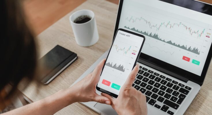 Person looking at charts on phone and laptop.