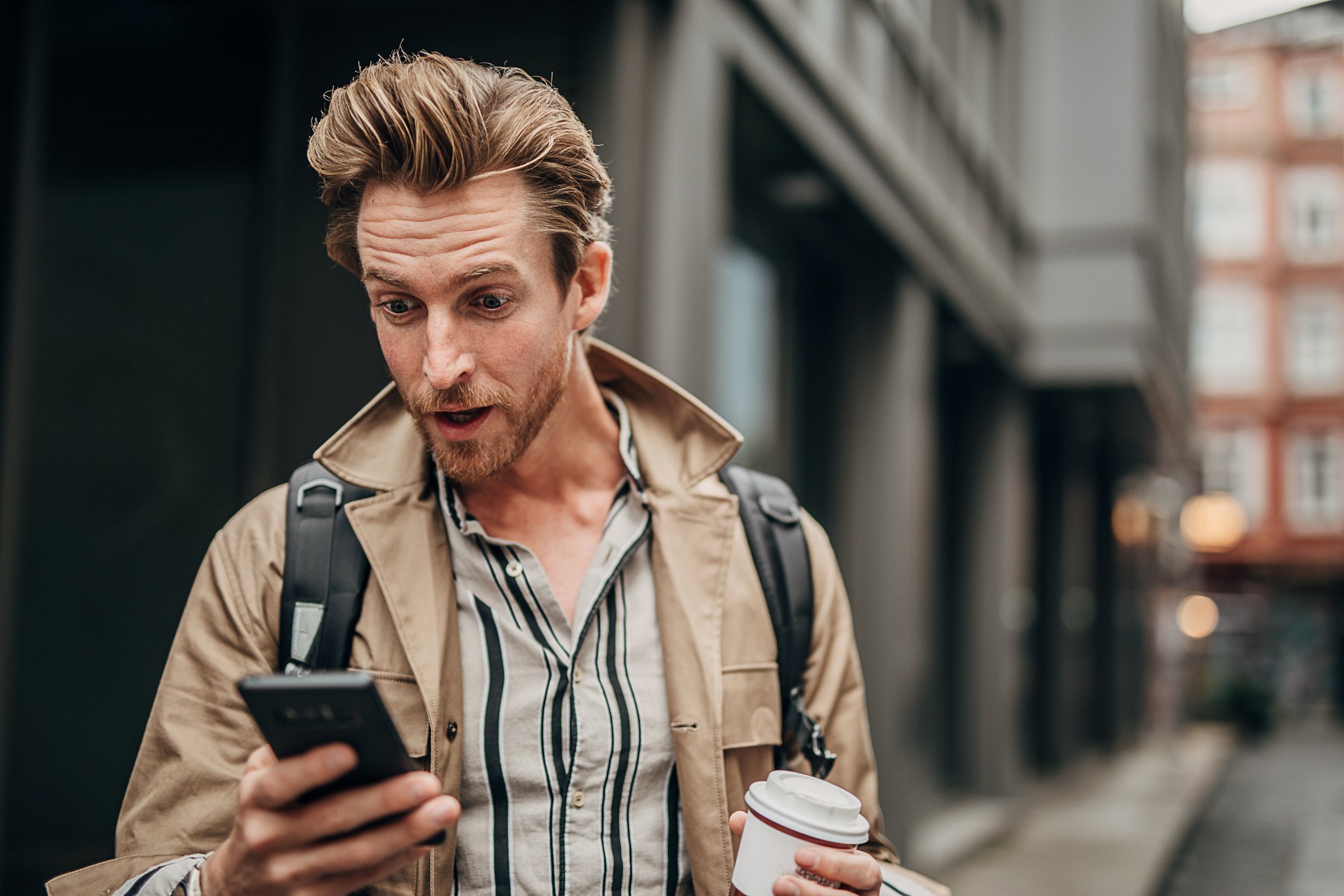 Una persona en la calle, mirando el teléfono con expresión sorprendida.