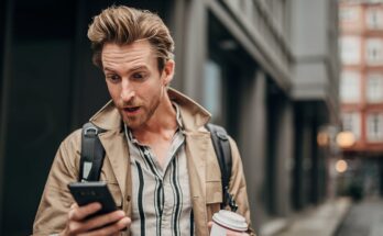 Person on street, staring at phone with surprised look.