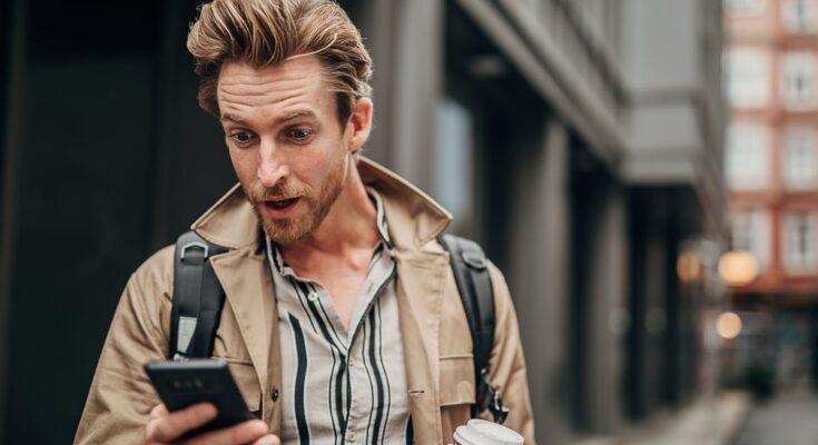 Person on street, staring at phone with surprised look.