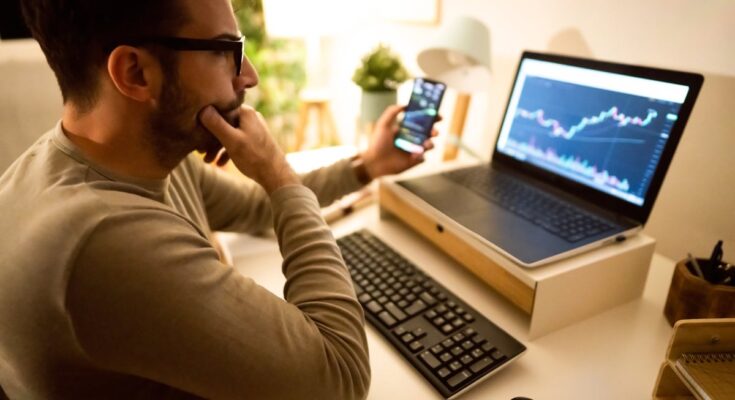 Person looking at a chart on their computer screen while holding a smartphone.