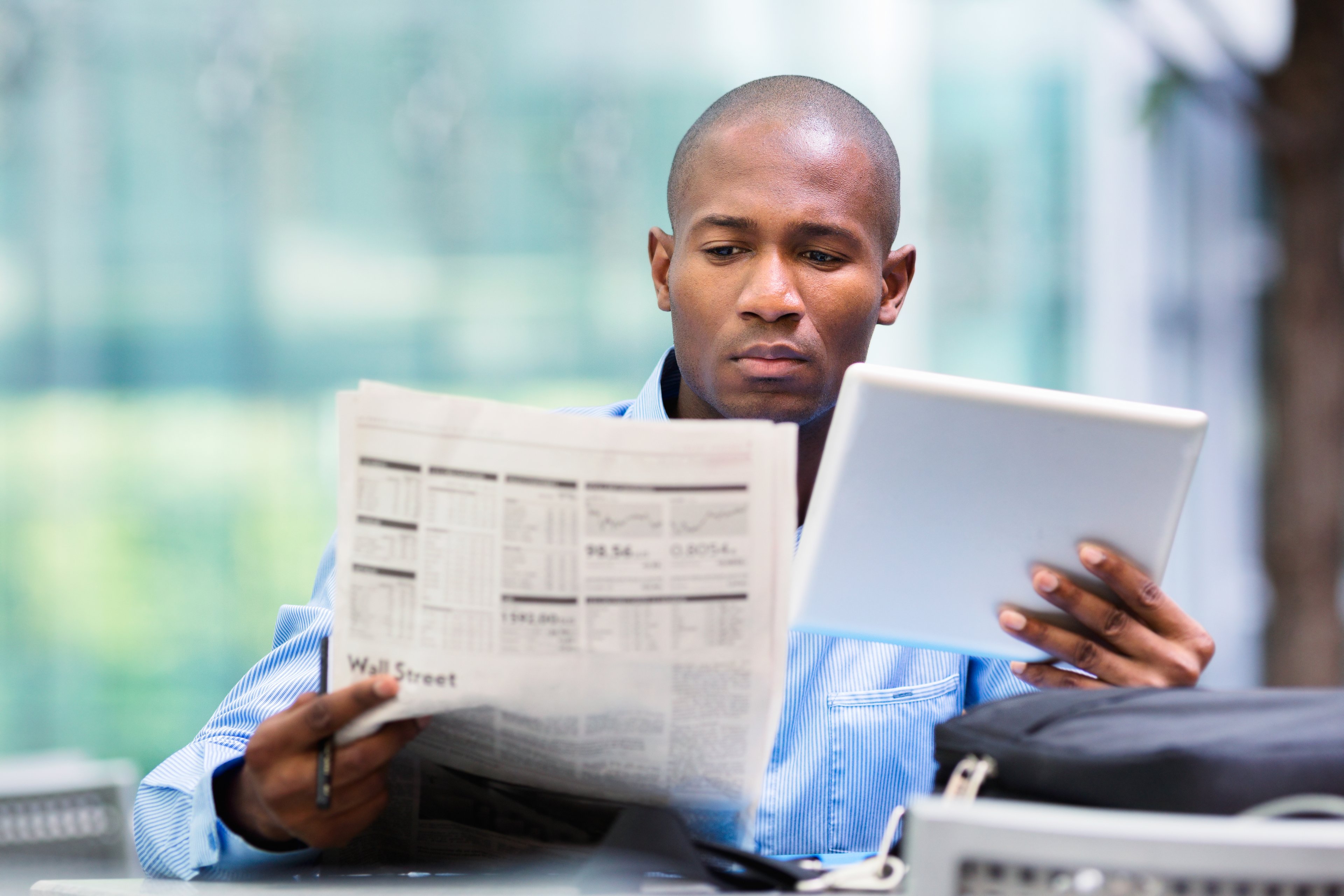 Persona mirando tableta y periódico financiero.