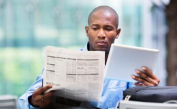 Person looking at tablet and financial newspaper.