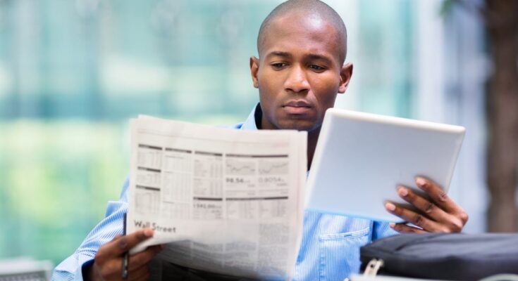 Person looking at tablet and financial newspaper.