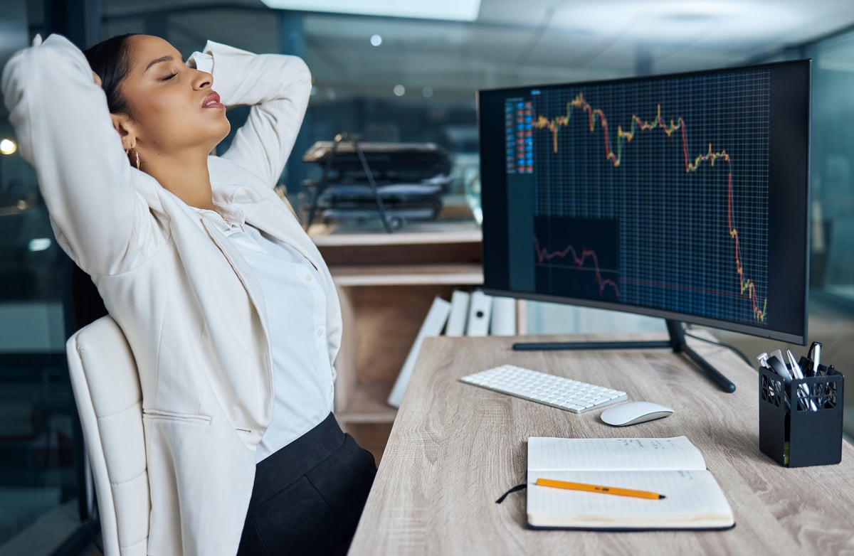 Persona de negocios decepcionada sentada frente al monitor con un gráfico de precios en caída.
