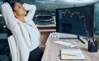 A disappointed business person sitting in front of a monitor with a falling price chart.