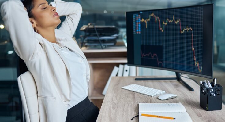 A disappointed business person sitting in front of a monitor with a falling price chart.