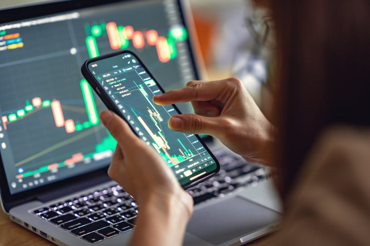 Persona analizando el gráfico de precios en una computadora portátil y un teléfono inteligente.