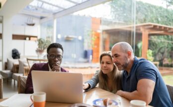 Three investors sit around a table at a cafe as one presents information on a laptop to the other two.