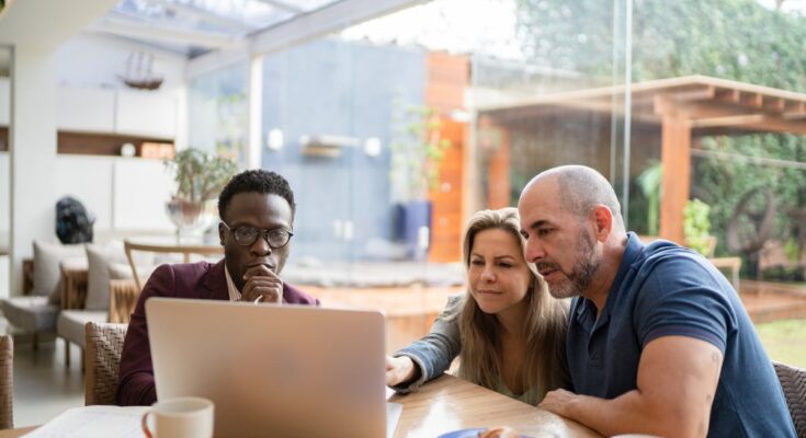 Three investors sit around a table at a cafe as one presents information on a laptop to the other two.