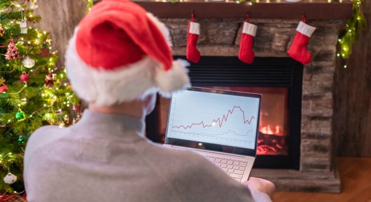 Holiday investor with laptop in front of fireplace.