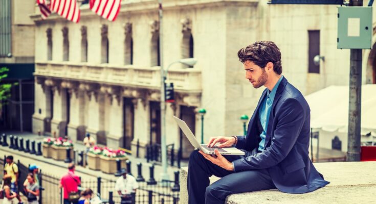 Trader with laptop on Wall Street.