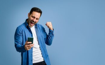 Investor in denim shirt and T-shirt doing a fist pump with smartphone.