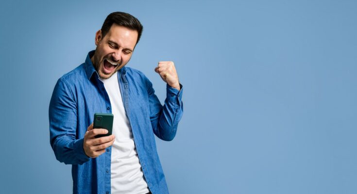 Investor in denim shirt and T-shirt doing a fist pump with smartphone.