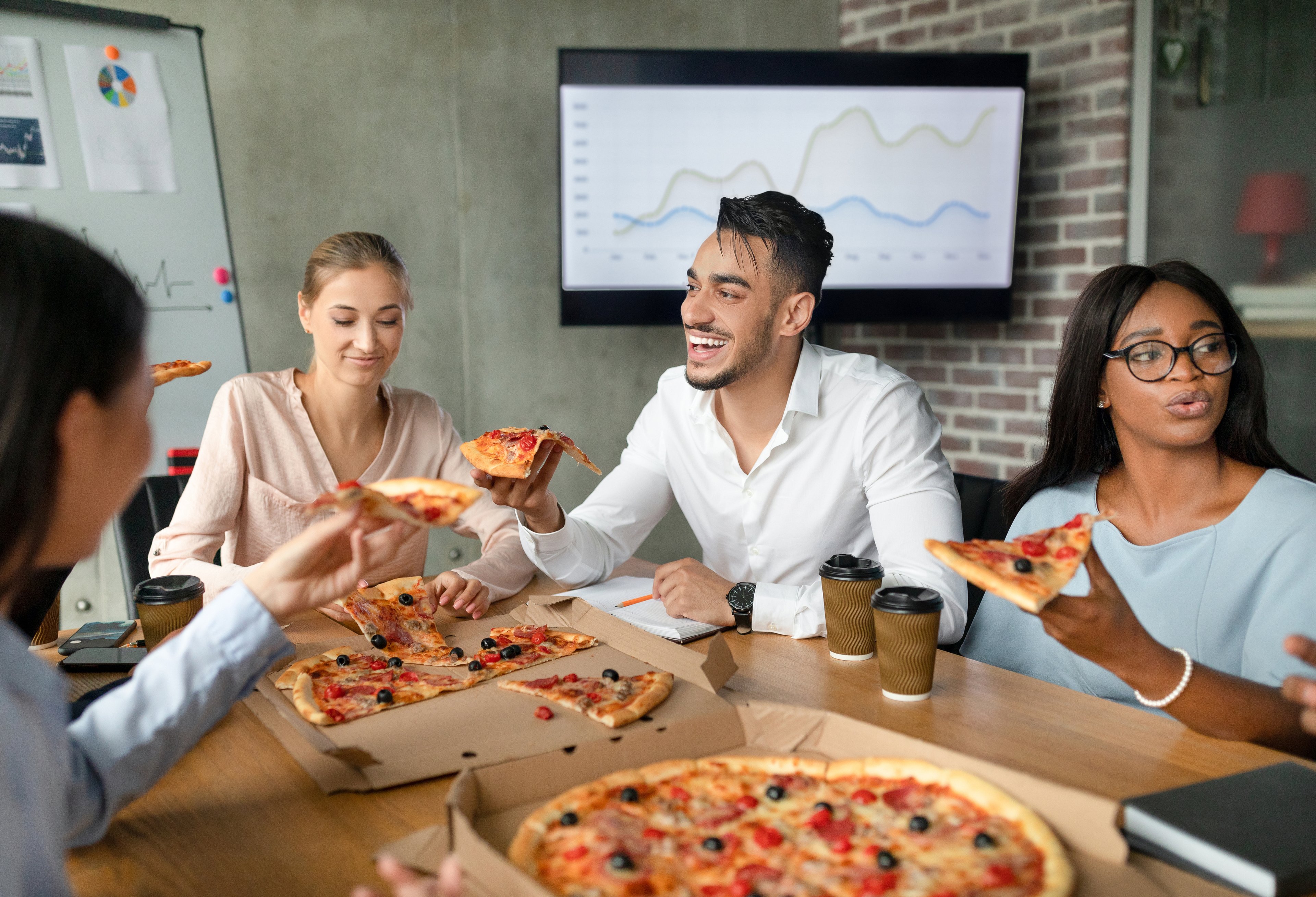 Los empleados comen pizza sentados en una mesa grande en una sala de conferencias.