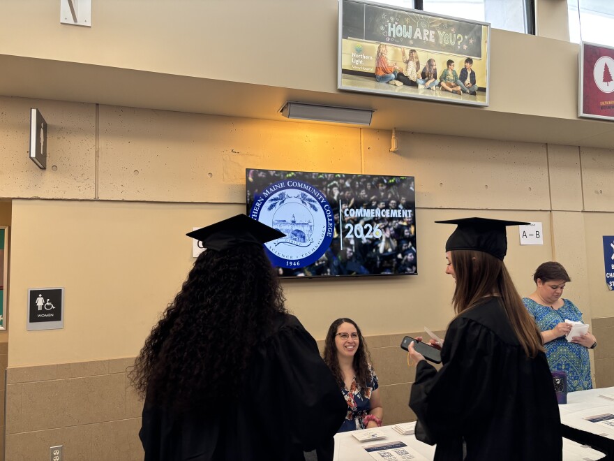 Dos graduados de Southern Maine Community College toman sus materiales finales antes de cruzar el escenario.