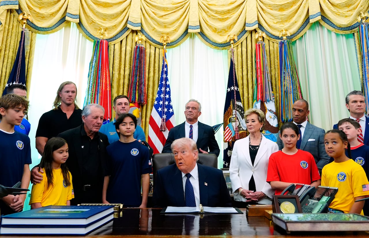 Donald Trump está sentado en su escritorio del Despacho Oval rodeado de niños y varios miembros de su gabinete.