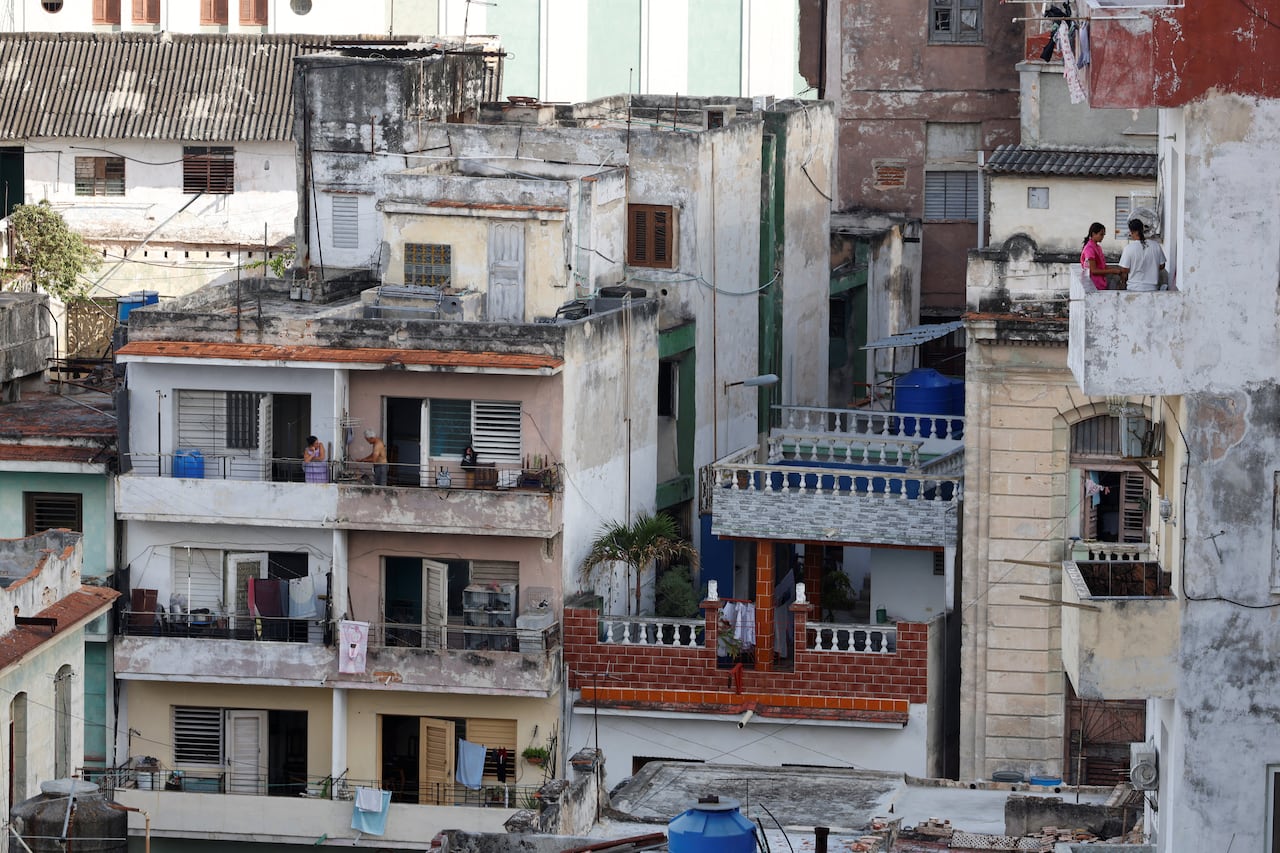 Una vista de una hilera de edificios en Cuba, con personas visibles de pie en los balcones en la imagen.